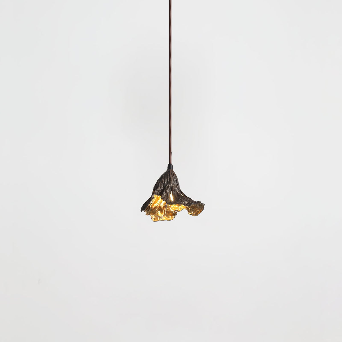 A small Clérachic pendant with a dark ruffled shade and gold interior hangs from a thin cord against a pale backdrop.