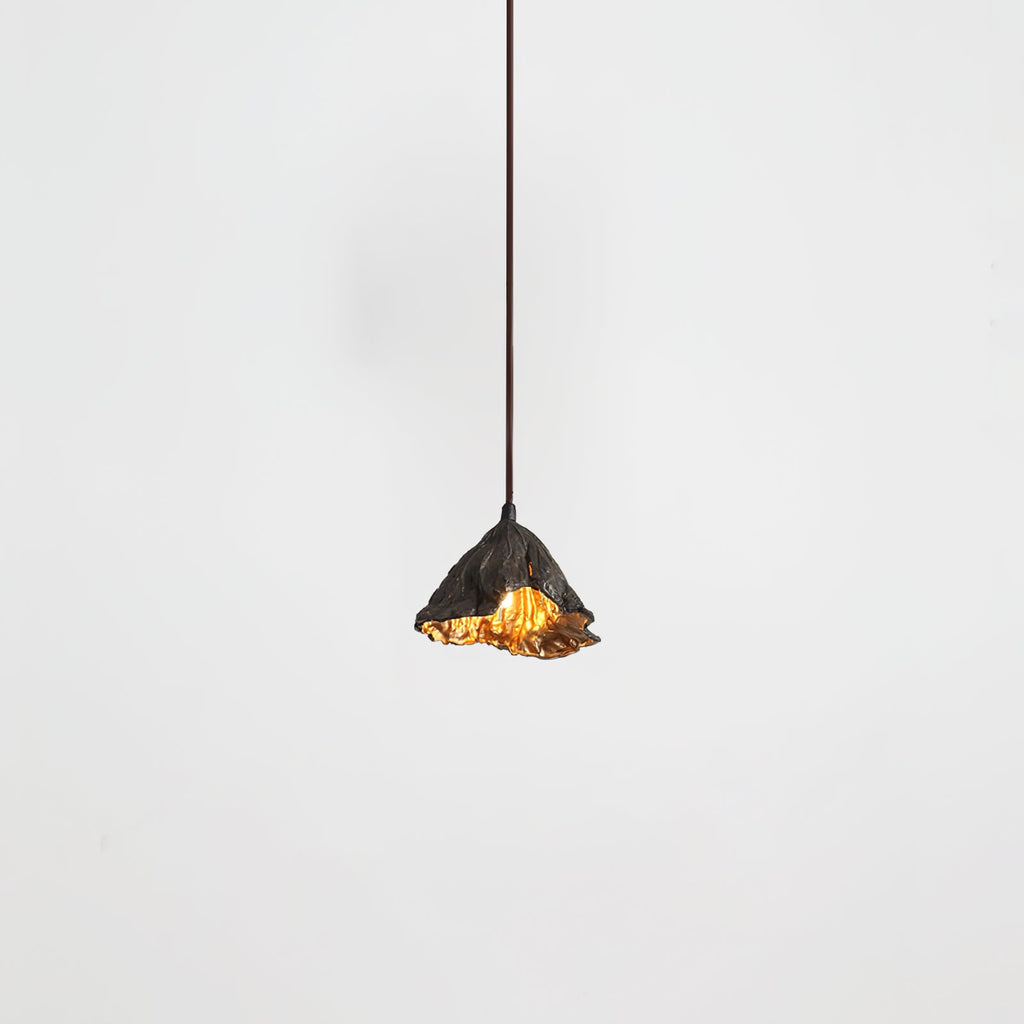 A Clérachic pendant with a ruffled black shade hangs from a thin cord, its gold interior just visible, on a pale backdrop.
