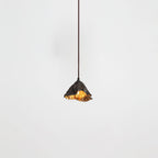 A Clérachic pendant with a ruffled black shade hangs from a thin cord, its gold interior just visible, on a pale backdrop.