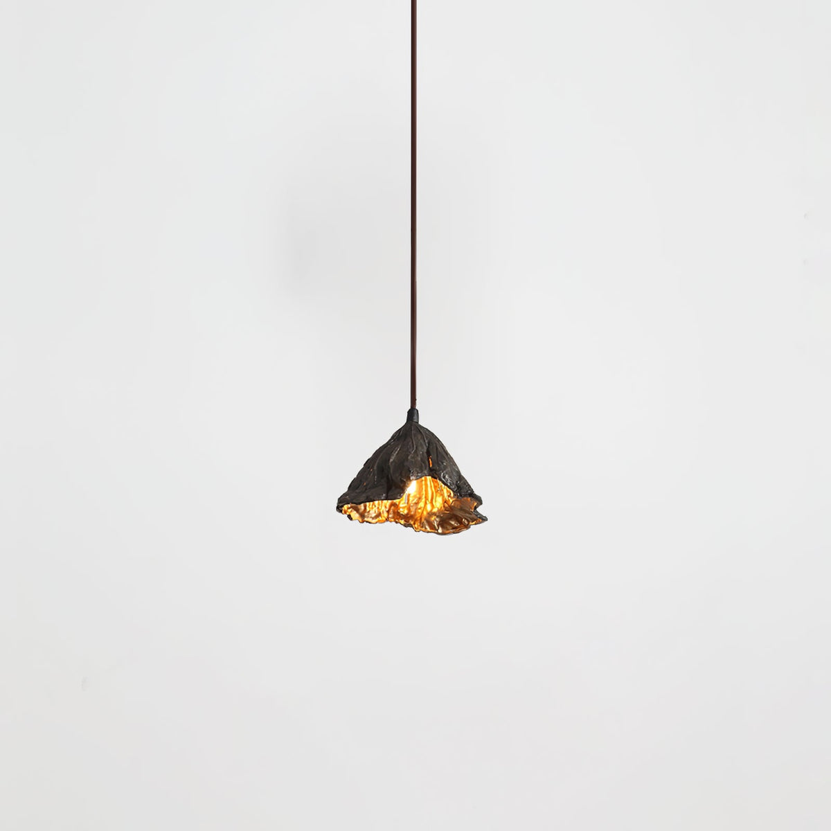 A Clérachic pendant with a ruffled black shade hangs from a thin cord, its gold interior just visible, on a pale backdrop.