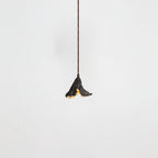 A small Clérachic pendant with a dark crinkled shade hangs from a thin cord, seen on a pale backdrop.