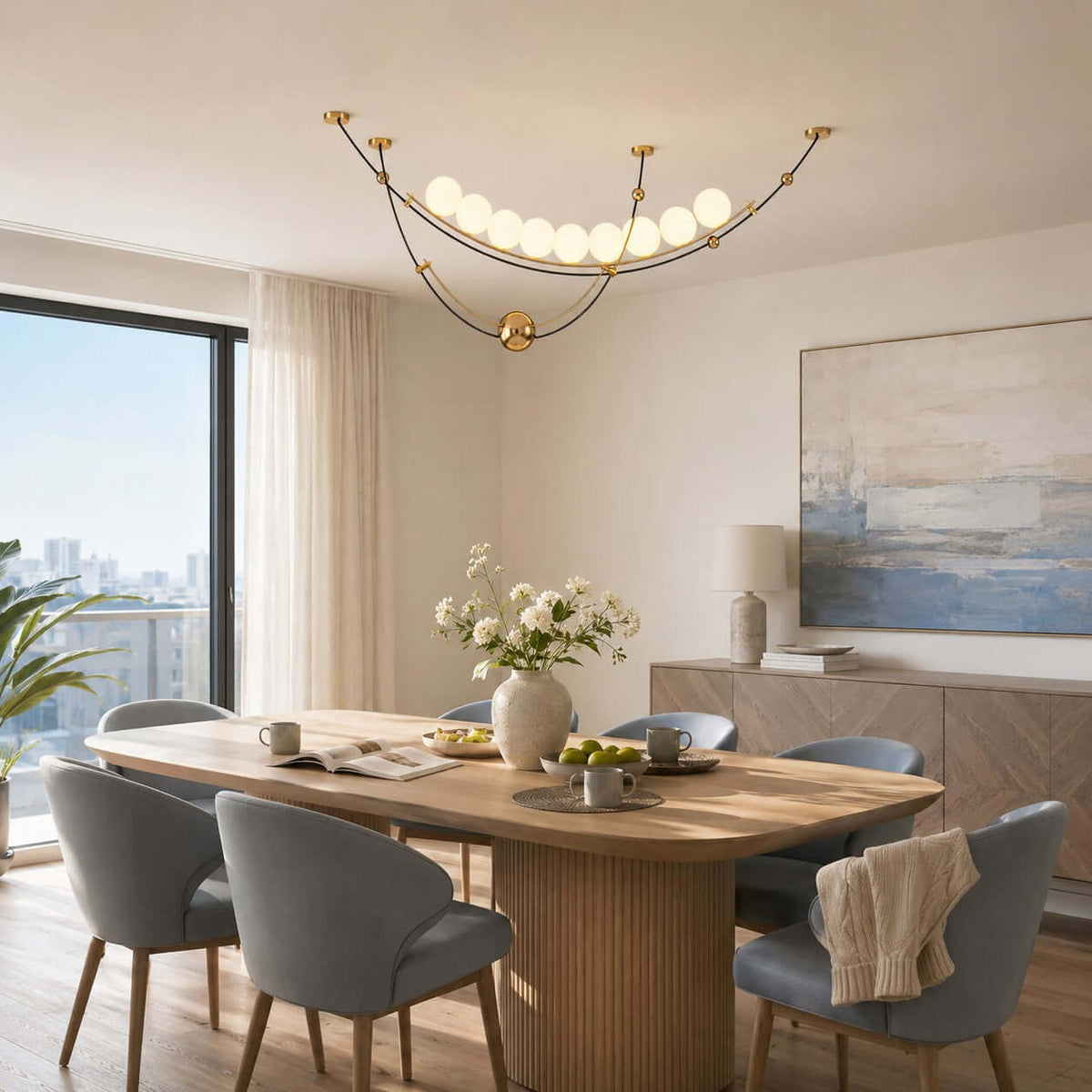 Lit Clérachic pendant with curved black and gold arcs over an oak dining table, with blue-grey chairs and a window onto the city.
