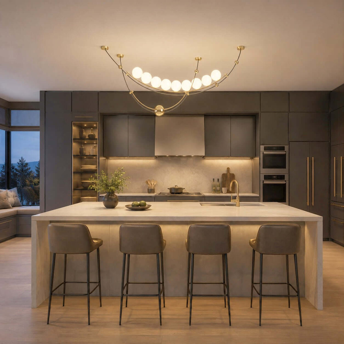 Above a pale stone island with four stools, this Clérachic pendant glows in a dark grey kitchen with a dusk view outside.