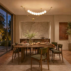 Clérachic pendant lit warmly over a wooden dining table laid for a meal, with green chairs and a marble alcove behind.