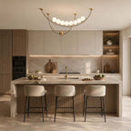A Clérachic pendant with white globes on gold-toned arcs, over a fluted-front kitchen island with three grey bar stools.