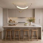 Clérachic pendant above a light kitchen island with four wooden stools, a bowl of green apples and a vase on the worktop.