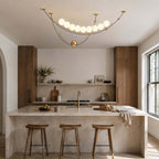 Lit Clérachic pendant in a bright kitchen with an arched doorway, above a stone island with three wooden stools.