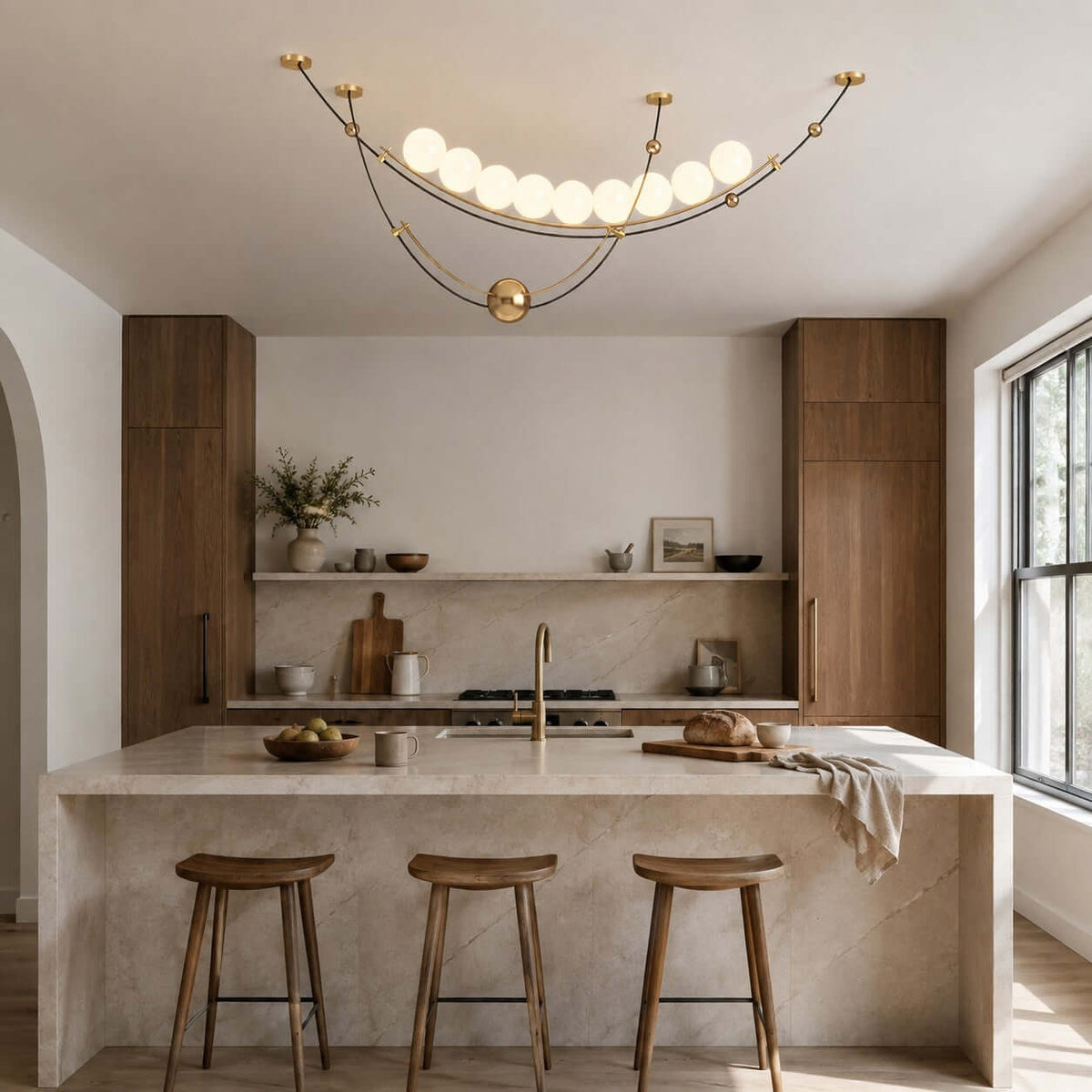 Lit Clérachic pendant in a bright kitchen with an arched doorway, above a stone island with three wooden stools.