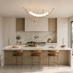 A Clérachic pendant centred over a kitchen island with a marble top, a fluted base and three tan leather stools.