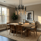 A Clérachic tubular chandelier lights a rustic wooden dining table with woven leather chairs, beside a tall leafy plant.