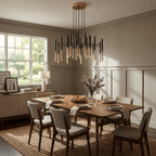 Below a panelled wall and a bright window, a Clérachic tubular chandelier hangs over a laid dining table with grey chairs.