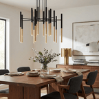 Black-and-gold tubes of a Clérachic chandelier hang above a walnut dining table, with an abstract painting and a brass vase behind.