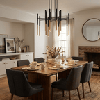 A Clérachic tubular chandelier hangs in a dining room with a brick fireplace, a round mirror and dark grey chairs.