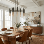 A Clérachic tubular chandelier hangs in a dining room with a coffered ceiling, over a wooden table and tan leather chairs.