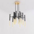 A Clérachic chandelier with black arms and gold-finish tubes hangs from the ceiling of a plain white room, seen from below.