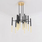 A Clérachic chandelier with black arms and gold-finish tubes hangs from the ceiling of a plain white room, seen from below.