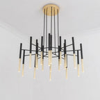 This Clérachic chandelier hangs low in a white room, with gold-finish tubes beneath black arms and a round brass-finish canopy.