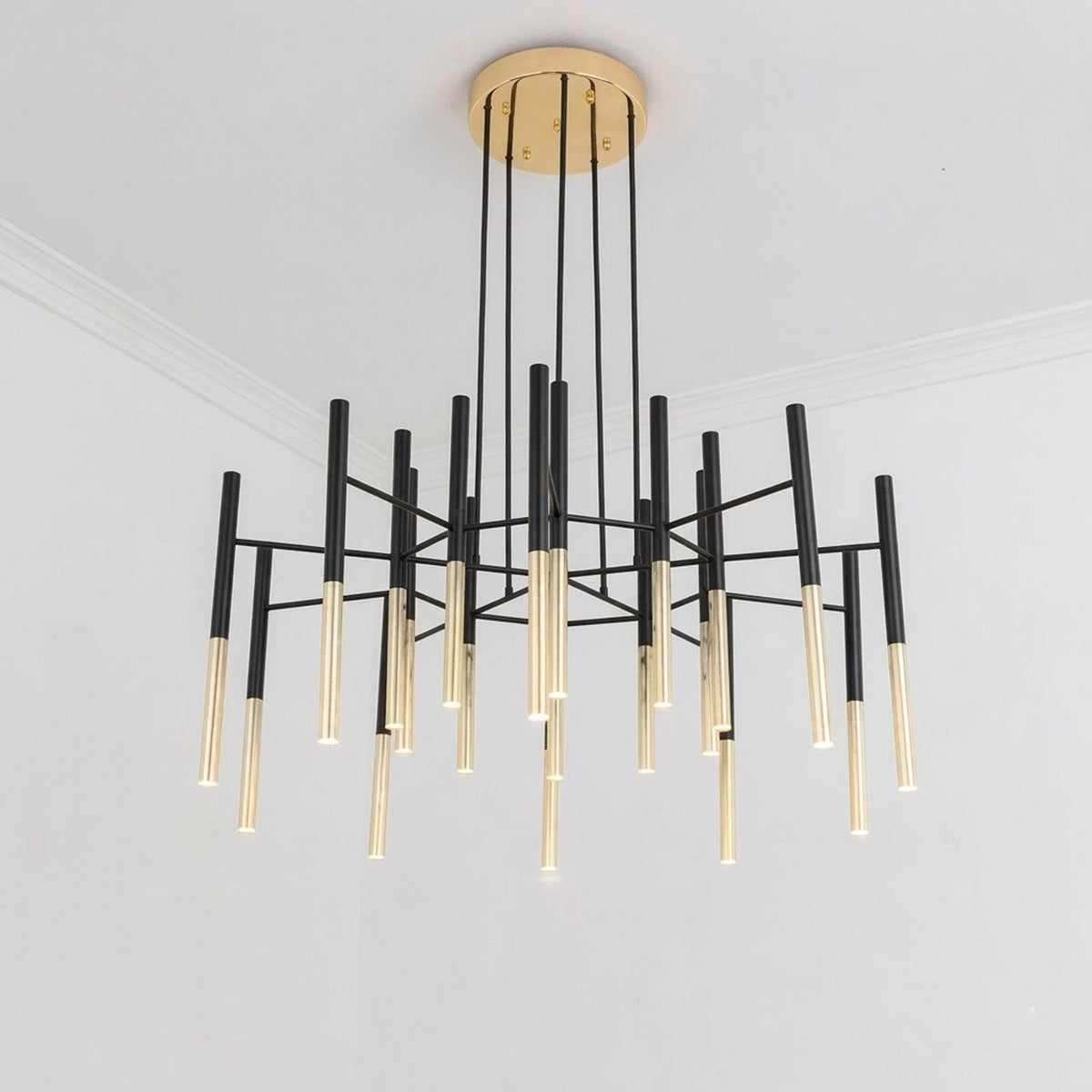 This Clérachic chandelier hangs low in a white room, with gold-finish tubes beneath black arms and a round brass-finish canopy.