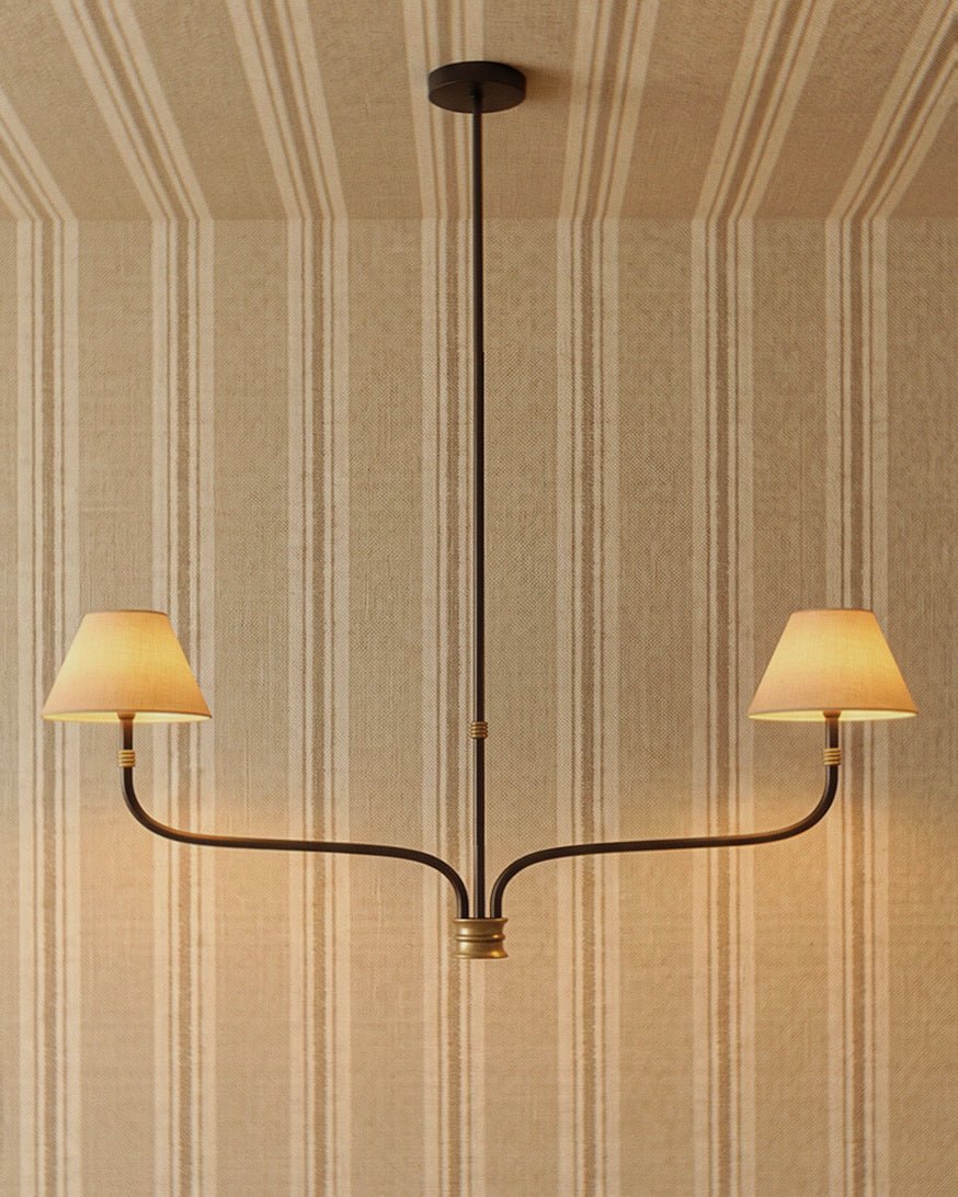 Clérachic two-arm chandelier in black iron with brass collars and cream fabric shades, glowing against a striped wall.