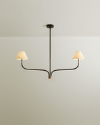 Clérachic chandelier with two sweeping black arms, a slim central stem and cream linen shades on a plain pale wall.