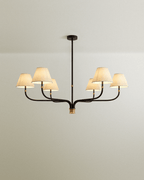 Clérachic six-arm chandelier in black iron with brass details and six cream linen shades, seen against a soft pale wall.