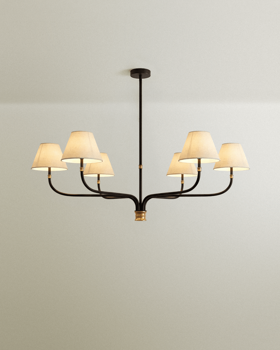 Clérachic six-arm chandelier in black iron with brass details and six cream linen shades, seen against a soft pale wall.