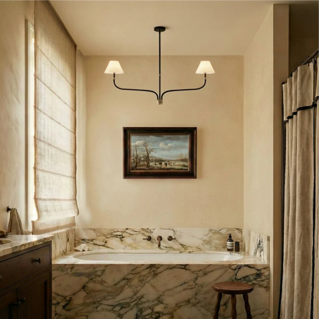Clérachic two-arm chandelier hung in a calm cream room above a framed landscape painting, with linen drapes at the window.