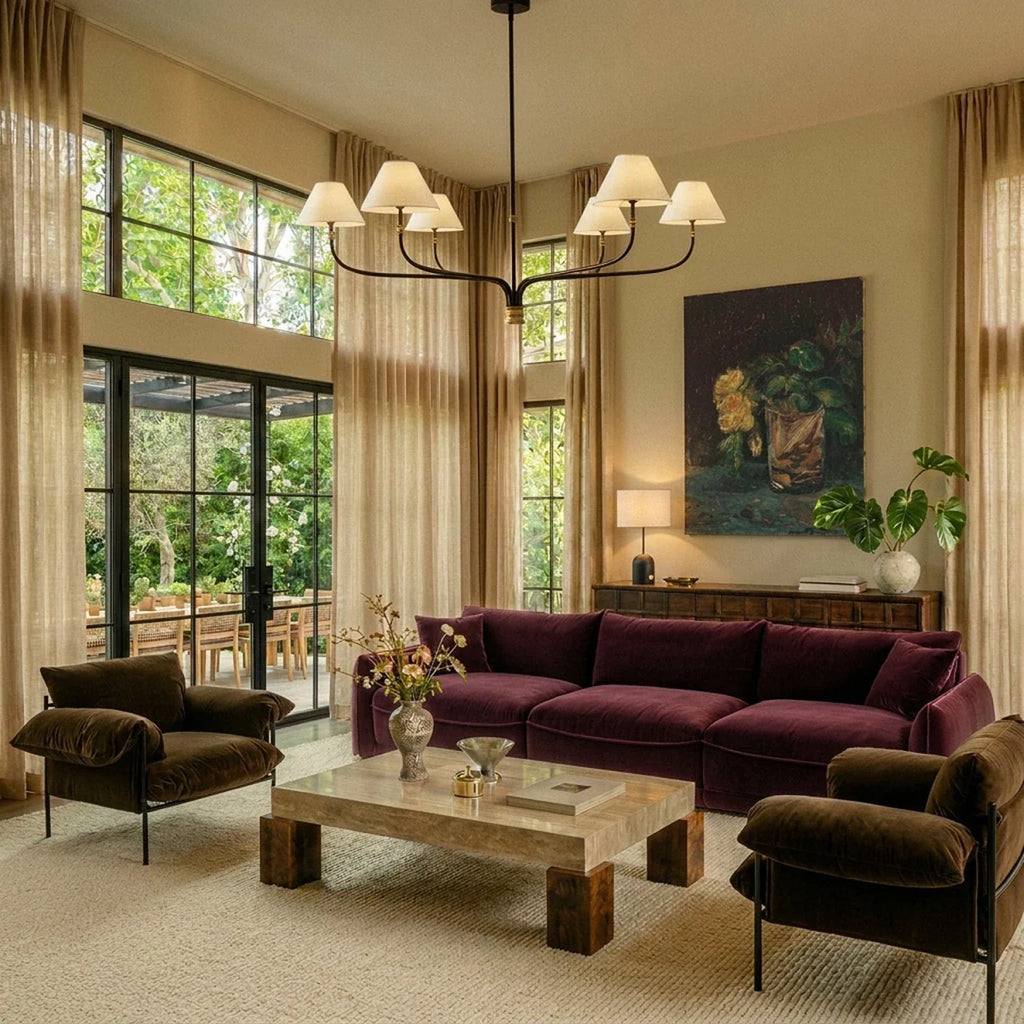 Clérachic six-arm chandelier over a plum velvet sofa in a tall living room with sheer curtains and glazed doors.