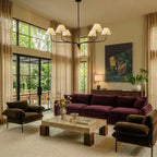 Clérachic six-arm chandelier over a plum velvet sofa in a tall living room with sheer curtains and glazed doors.