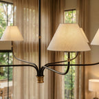 Close view of a Clérachic chandelier shade in textured cream linen, with black iron arms and a brass collar behind it.