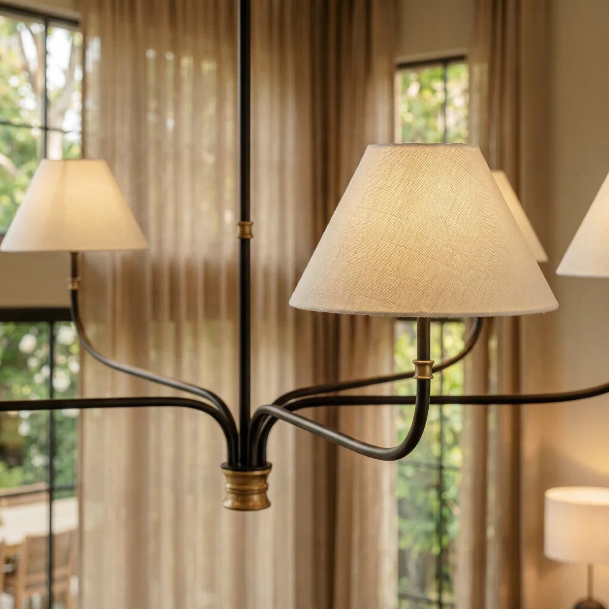 Close view of a Clérachic chandelier shade in textured cream linen, with black iron arms and a brass collar behind it.