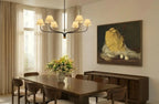 Clérachic six-arm chandelier hanging above a walnut dining table, with sheer curtains and a large still-life painting.