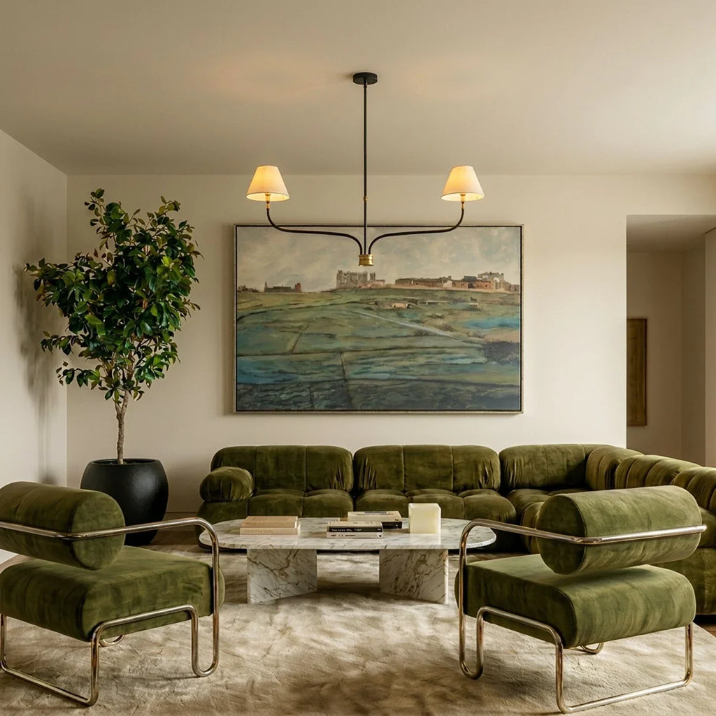 Clérachic two-arm chandelier over a green velvet sofa and marble coffee table, in front of a large landscape painting.
