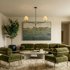 Clérachic two-arm chandelier over a green velvet sofa and marble coffee table, in front of a large landscape painting.