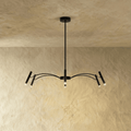 A matte black iron chandelier with slender branching arms and cylindrical heads hangs against a plaster wall, Clérachic hero shot.