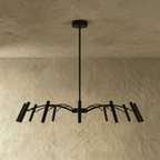 A denser black iron chandelier shows cascading arms and tube heads fanning broadly beneath a plaster ceiling, Clérachic hero shot.