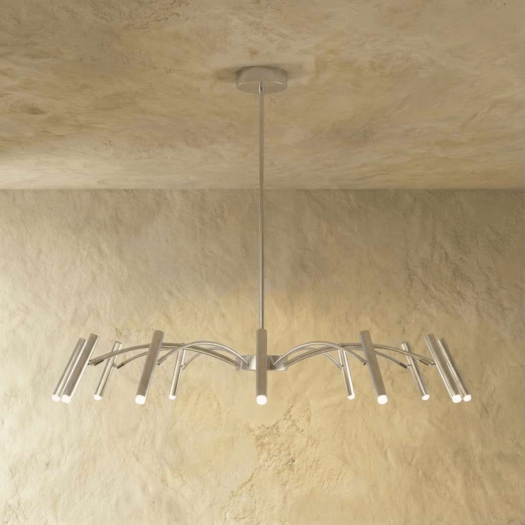 A brushed silver-toned chandelier shows its arched arms and cylindrical heads catching warm light in this Clérachic hero shot.