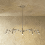 A brushed silver-toned chandelier shows its arched arms and cylindrical heads catching warm light in this Clérachic hero shot.