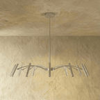 The silver-toned chandelier's compact arm spread and tube heads are shown straight-on against a plaster wall in this Clérachic hero shot.