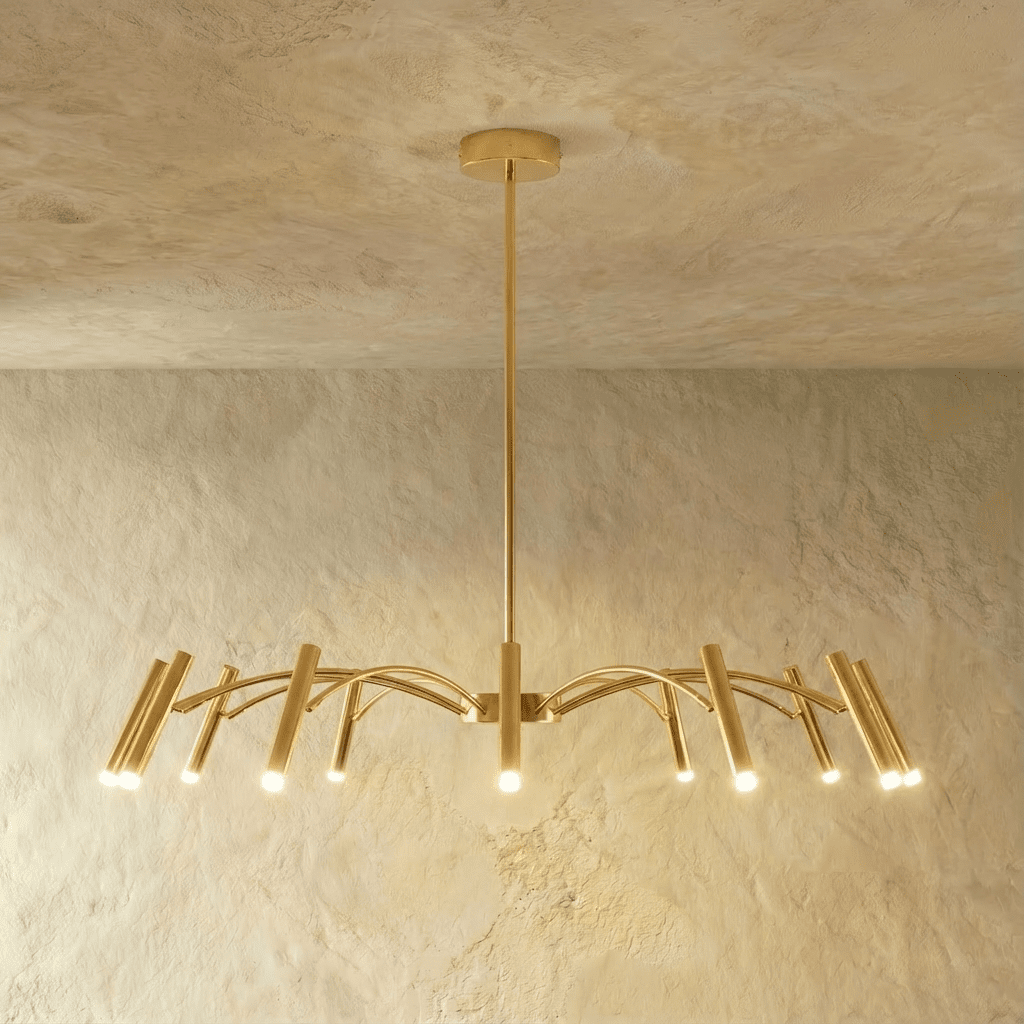 The brass-toned chandelier's arms glow warm at each cylindrical head, spread mid-width against a plaster wall in this Clérachic hero shot.