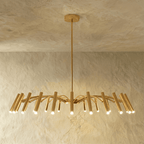 A fuller brass-toned chandelier spreads its arched arms and many lit cylindrical heads wide across the frame, Clérachic studio hero shot.