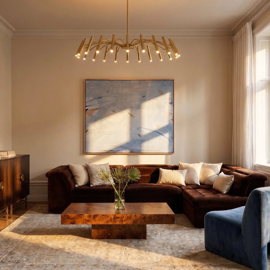 The brass-toned chandelier hangs above a velvet sectional and abstract art in a warm living room styled by Clérachic.