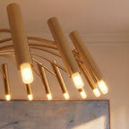 A close-up on the brass-toned chandelier's cylindrical heads and glowing bulbs, framed against art and window light, Clérachic detail shot.