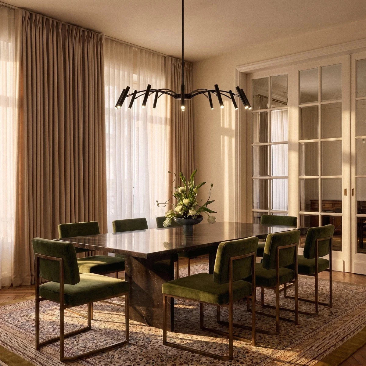 The black iron chandelier hangs low over a marble dining table and olive velvet chairs in a Clérachic dining room lifestyle shot.
