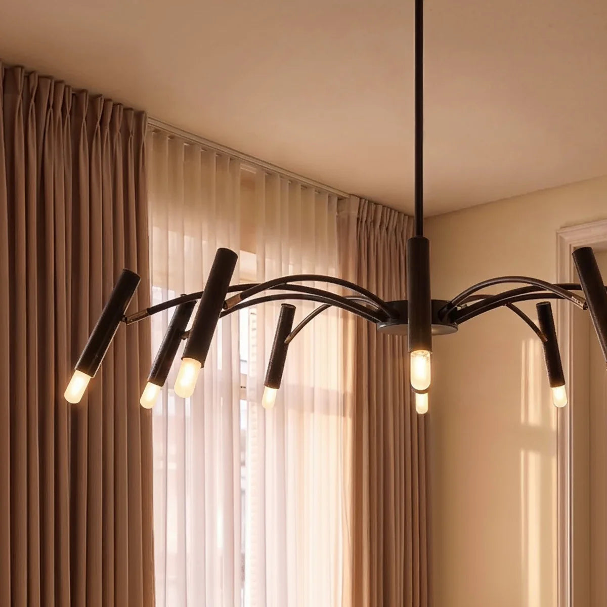 A close-up on the black iron chandelier's slender arms and glowing cylindrical heads against sheer curtains, Clérachic detail shot.