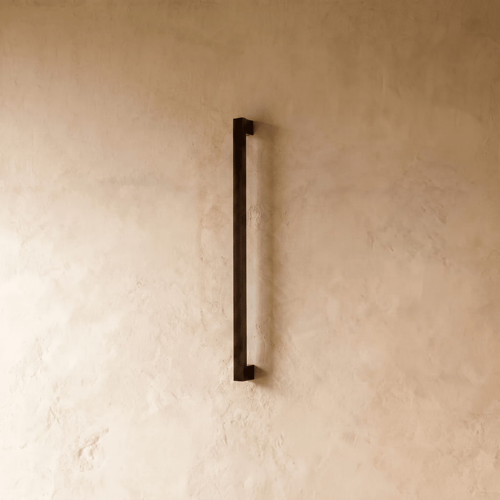 The slim black column wall light is shown unlit, its square profile against a plain plaster wall in this Clérachic hero shot.