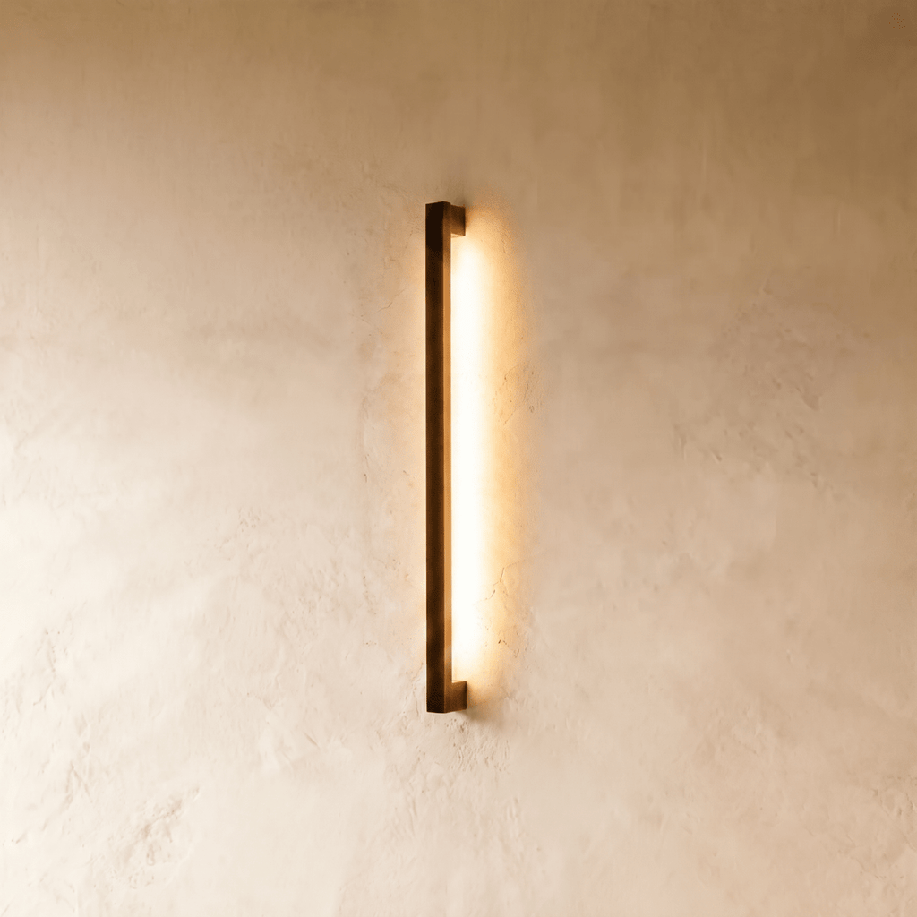 The slender black column wall light washes warm light down a plaster wall in this closer-angle Clérachic hero shot.