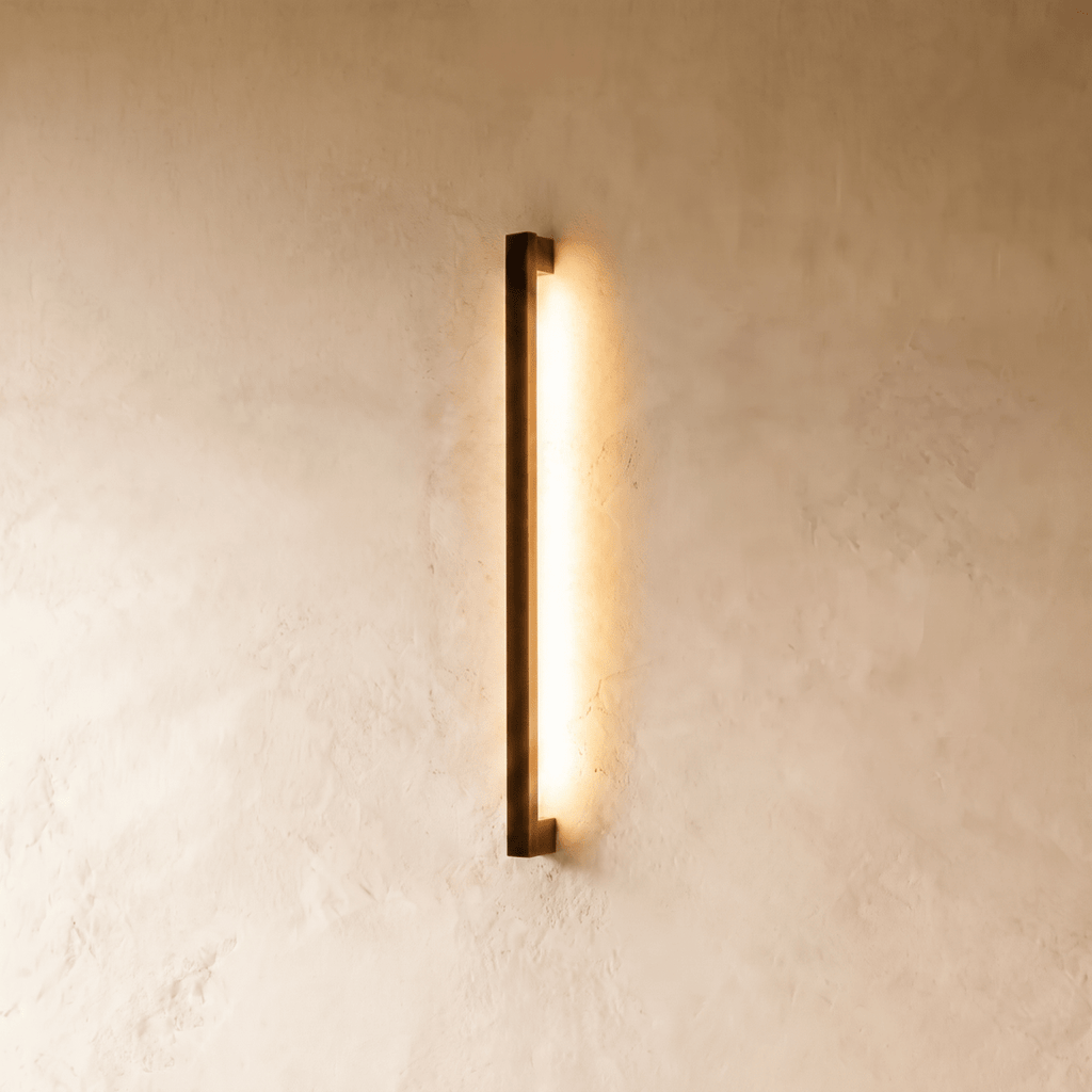 Another lit view of the black column wall light shows its warm glow spreading evenly down the plaster wall in this Clérachic hero shot.
