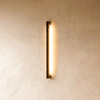 Another lit view of the black column wall light shows its warm glow spreading evenly down the plaster wall in this Clérachic hero shot.
