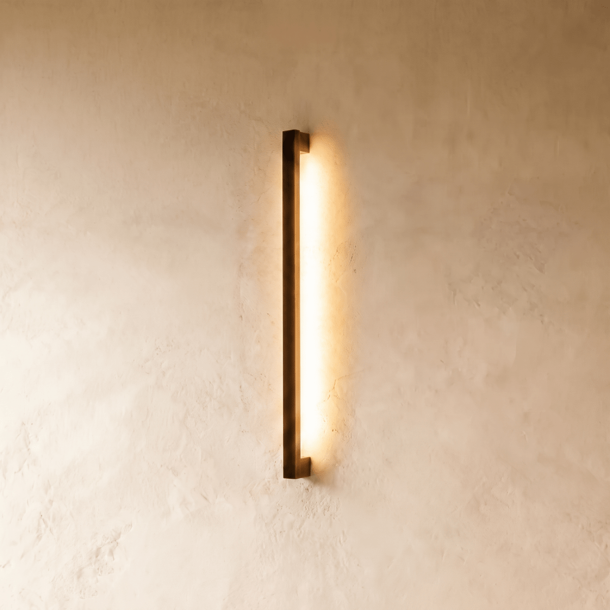 Another lit view of the black column wall light shows its warm glow spreading evenly down the plaster wall in this Clérachic hero shot.